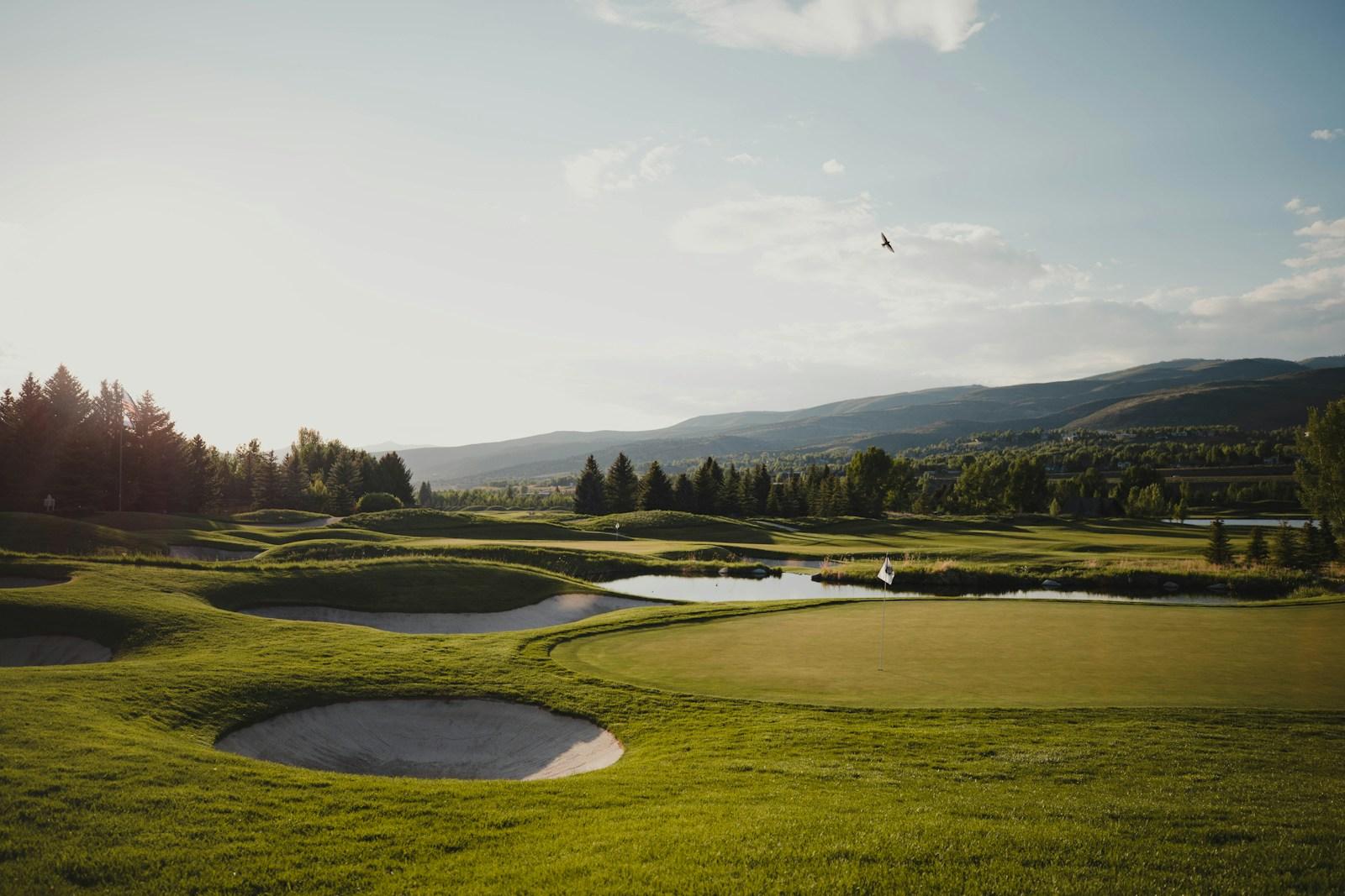 Golf course at golden hour with bunkers, flag, and mountain backdrop